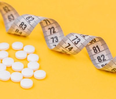 White measuring tape with a white pills, white vitamin on a yellow background. Diet. Slimming. Obesity. Place for an inscription. Weight loss marathon. Advertising. Top view. The close plan.