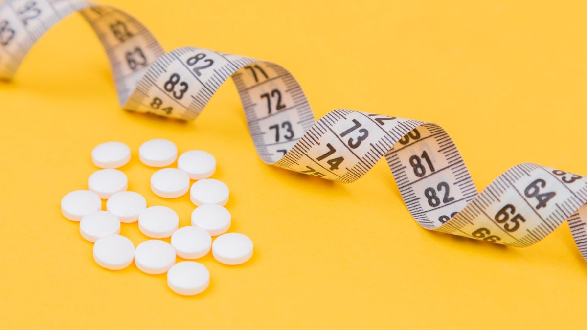 White measuring tape with a white pills, white vitamin on a yellow background. Diet. Slimming. Obesity. Place for an inscription. Weight loss marathon. Advertising. Top view. The close plan.