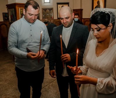 Bride and guests holding candles during an Orthodox wedding ceremony in a church setting.