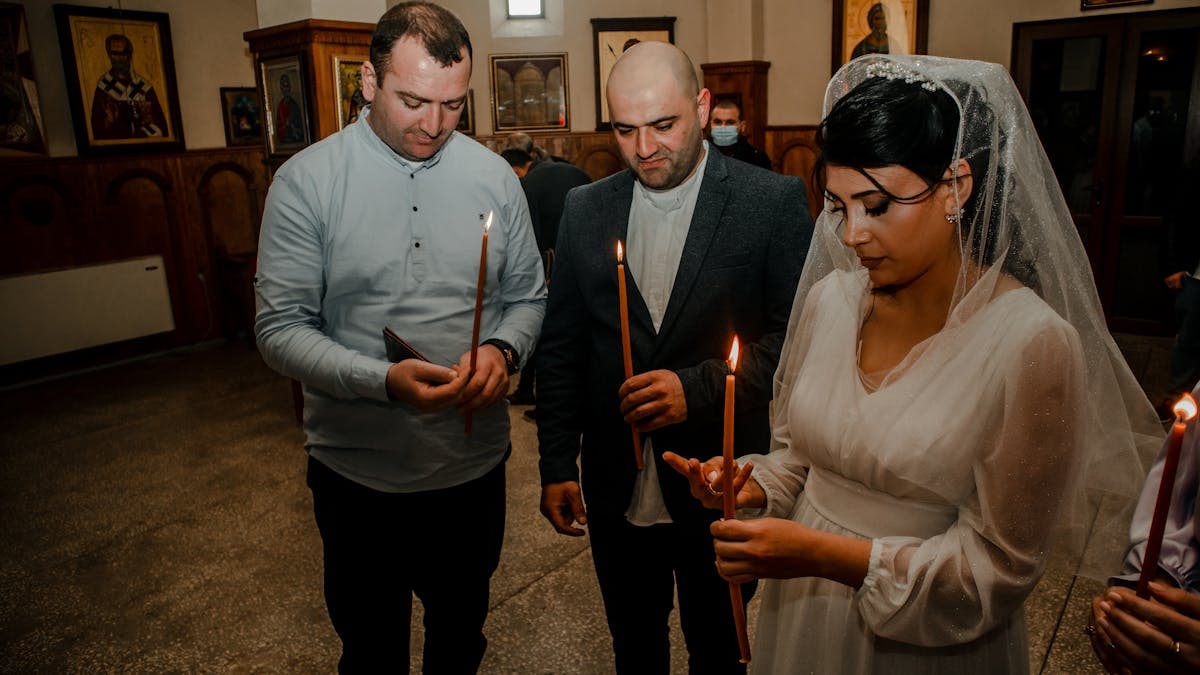 Bride and guests holding candles during an Orthodox wedding ceremony in a church setting.